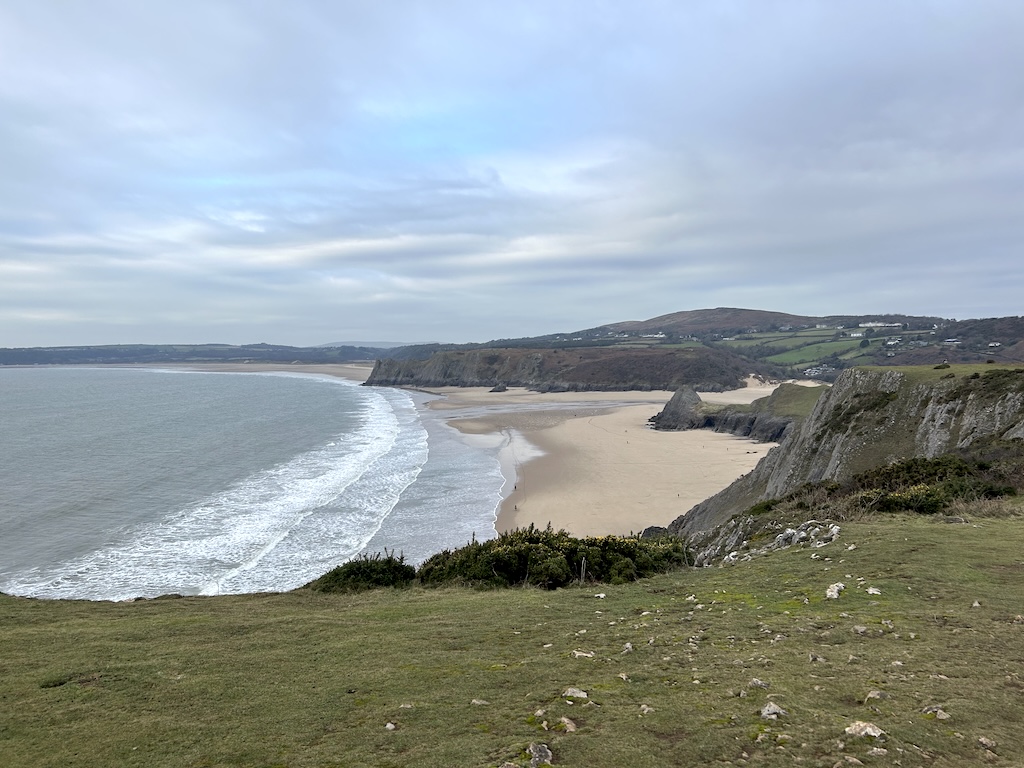 Looking down from a grassy cliff top to a huge sweeping sandy bay.